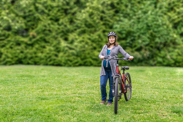 pregnant woman on the green lawn in a park holding bicycle ready to ride.