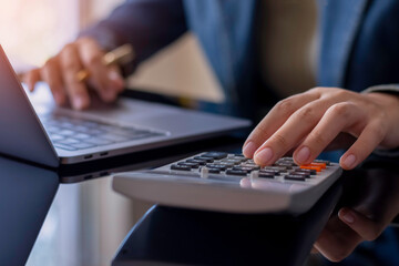 Business woman hand using calculator and working on laptop computer at office.