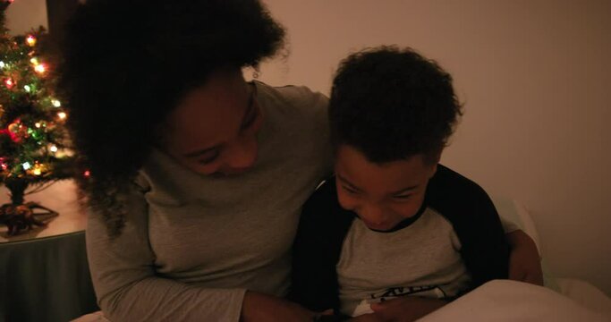 MS HANDHELD Mother playing with son (6-7) on bed at Christmas tree / Dinton, Wiltshire, UK