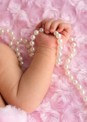 Newborn baby hand holding pearls