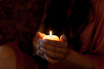 Candle in female hands on black background.