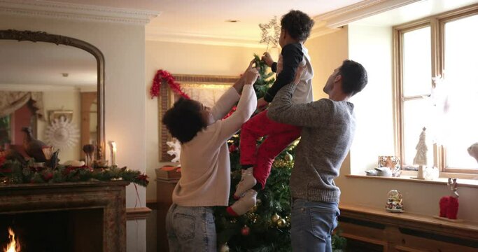 MS TU Family with son (6-7) putting star in top of Christmas tree in living room / Dinton, Wiltshire, UK