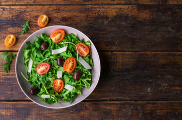 Salad bowl with arugula rocket salad, black olives, cherry tomatoes, and hard cheese. Concept of healthy, vegetarian and vegan food