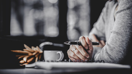Woman holding pen on notebook with coffee cup on table