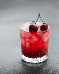 Fresh summer cocktail with cherry and ice cubes. Glass of cherry drink on dark background. Selective focus