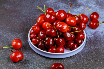 Natural shiny cherries with stem in plate.