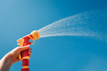 Hand holds yellow hose with nozzle on background of blue sky with water splashes