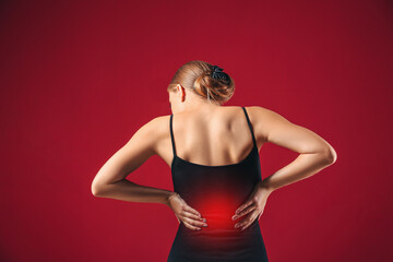 Young woman suffering from back pain on color background