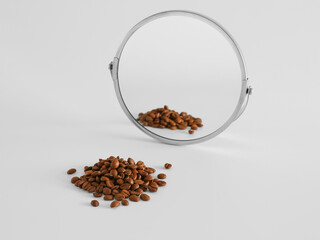 Coffee beans near mirror on light background