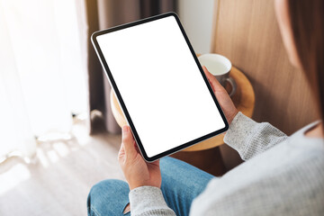 Top view mockup image of a woman holding black tablet pc with blank desktop white screen while sitting on a cozy white bed at home