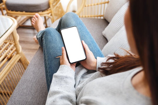 Top view mockup image of a woman holding mobile phone with blank desktop white screen while lying on a sofa at home