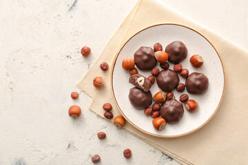 Plate with tasty chocolate candies and nuts on white background