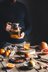 A man pours citrus tea on a wooden table. Healthy drink, vintage style. Vegan, eco products.