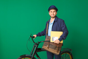 Handsome young postman with bicycle on color background