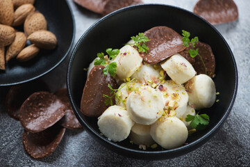 Cottage cheese dumplings served with chocolate chips and nuts in a black bowl, selective focus, horizontal shot