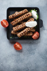 Above view of bbq balkan cevapi or skinless beef sausages with kaymak cheese, vertical shot on a light-blue stone background with space