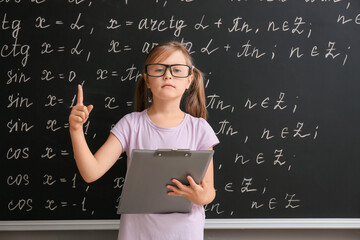 Cute little schoolgirl near blackboard in classroom