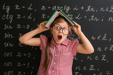 Funny little schoolgirl with book near blackboard in classroom