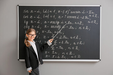 Cute little schoolgirl near blackboard in classroom