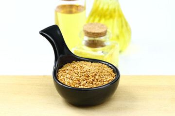 Flax seeds in a black ceramic bowl and flax seed oil in bottles on wooden board