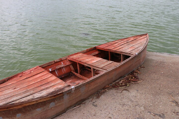 A wooden boat that is by the side of the pond