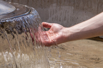 Hand cooling down in a stream of water from a city foutain in Tarnow, Poland. June 2020