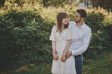 Fototapeta premium A guy and a girl kiss and walk in nature among the trees. Late evening romantic date at sunset.