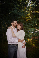 Fototapeta premium A guy and a girl kiss and walk in nature among the trees. Late evening romantic date at sunset.
