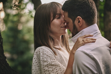 Fototapeta premium A guy and a girl kiss and walk in nature among the trees. Late evening romantic date at sunset.