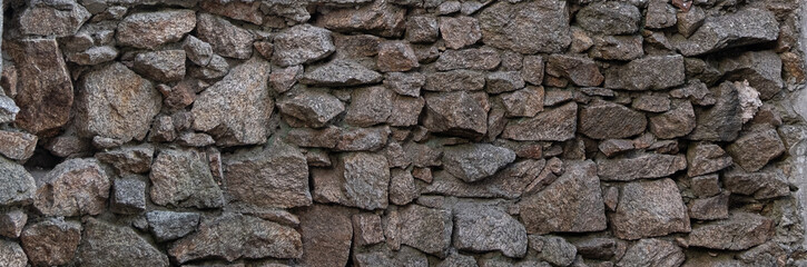 Old, rough stone wall made from rocks of different sizes. Wide background.