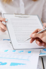 Female arm in suit offer contract form on clipboard pad and silver pen to sign closeup. Strike a...