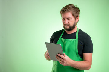 Supermarket employee with green apron and black t-shirt takes notes, looking at the camera