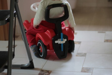 Fototapeta premium Small kid, child on a red car toy. Driving in the room alone.