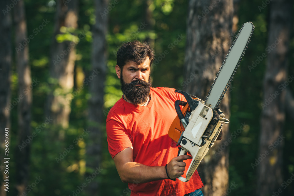 Wall mural handsome young man with axe near forest. deforestation. lumberjack in the woods with chainsaw axe. a