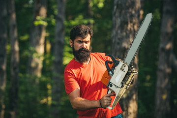 Handsome young man with axe near forest. Deforestation. Lumberjack in the woods with chainsaw axe....