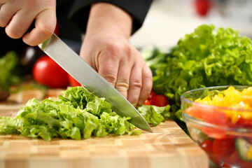 Cook holds knife in hand and cuts on cutting board green for salad or fresh vegetable soup with vitamins. Raw food and vegetarian recipe book in modern society popular concept.