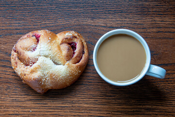A cup of coffee with fresh heart bun. Bakery on wooden background. Top view
