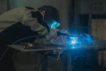 Industrial worker in protective mask using modern welding machine for welding metal construction on...