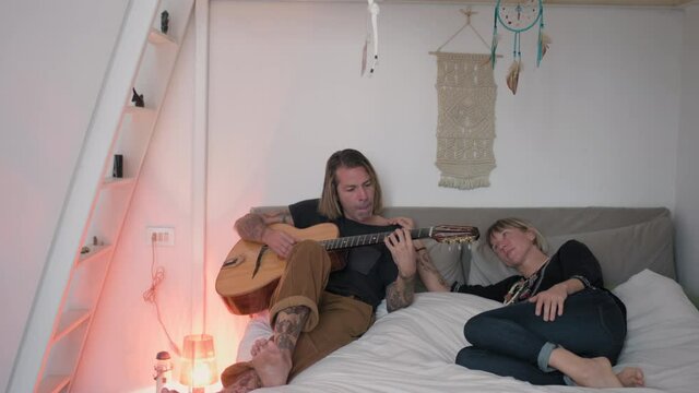 MS Woman embracing man playing acoustic guitar on bed / Milan, Italy