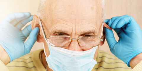 old man in sterile gloves fixes disposable mask on ears