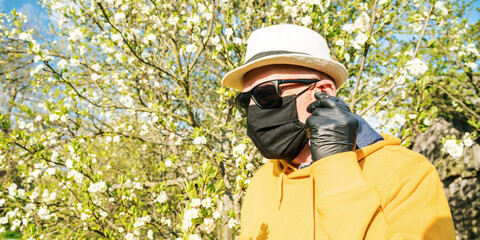 old man in mask puts on wireless headset in blooming garden
