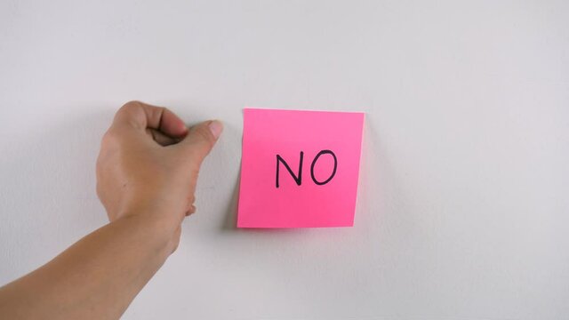 Closeup shot of woman's hand sticking note with "NO" word on a white background. Indian female's hand putting a handwritten pink sticky note reading "No" on a white wall - a reminder concept