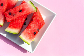Summer creative watermelon layout. Sweet red slices of  ripe watermelon on white plate on pink background. Healthy food summertime concept. Intarnational watermelon day.Copy space
