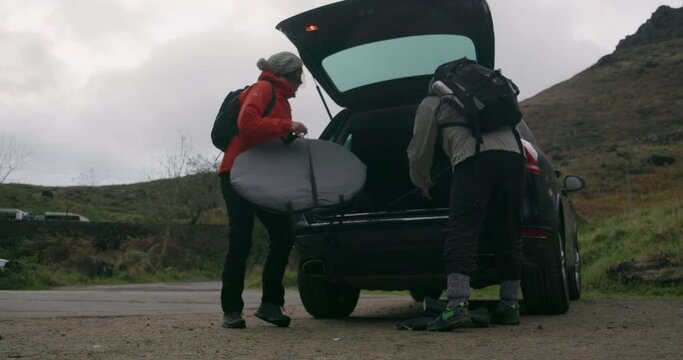 WS Rear view of man and woman loading camping equipment into car trunk / Yorkshire Moors, Yorkshire, UK