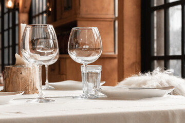Glasses, a plate, a knife, a candle are on a white tablecloth in a restaurant. Banquet hall, cafe for the celebration of the holiday. Dinner, breakfast and lunch in a stylish wooden interior. Close-up