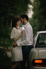 A guy and a girl are hugging next to a car. Romantic date evening walk. The relationship between people is love and tenderness.