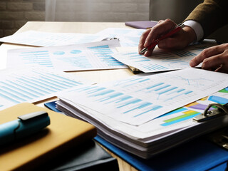 A pile of papers with data and graphs on the table. A man checks the financial statements.