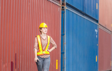 Woman engineer in hardhat and safety vest holding holding two-way radio control loading containers box from cargo