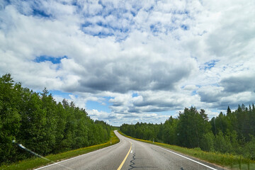 View from relief car windscreen on the blue sky with white clouds, grey asphalt road and landscape with forest and green teeses. Landscape through window