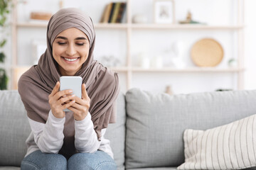 Cheerful Muslim Girl In Headscarf Spending Time At Home With Smartphone